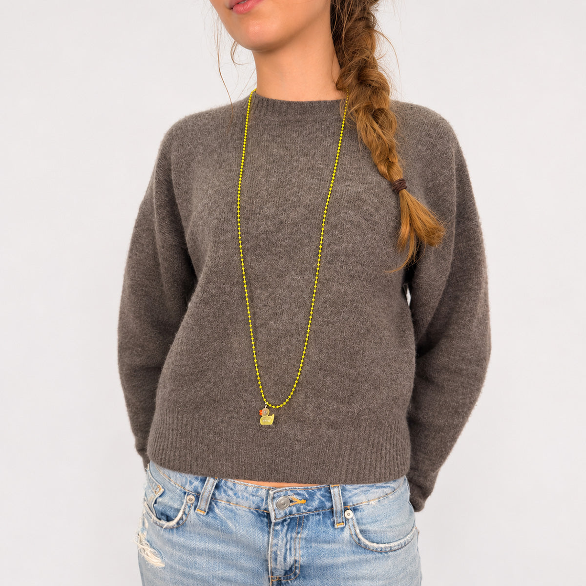 Gelbe Escapulario Entenkette mit fluoreszierendem Entenanhänger und orangefarbenem Schnabel, lässig gestylt zu Strickpullover und Jeans.