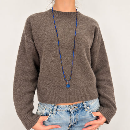 Lange dunkelblaue Kugelkette mit blauem fluoreszierendem Entenanhänger von Escapulario, getragen zu Strickpullover und Jeans.