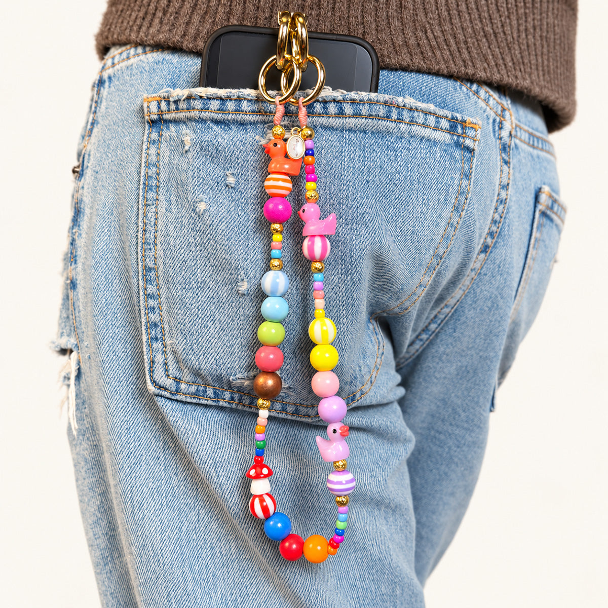 Kurze bunte Handykette mit orangefarbenem und pinkem Entchen, bunten Holz- und Acrylperlen sowie goldfarbenen Karabinerringen an einer Jeans.