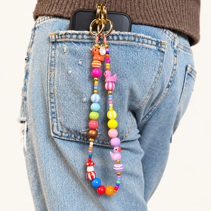 Kurze bunte Handykette mit orangefarbenem und pinkem Entchen, bunten Holz- und Acrylperlen sowie goldfarbenen Karabinerringen an einer Jeans.